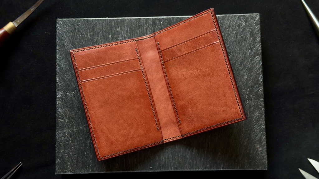 Brown leather wallet on a dark surface with tools in the background