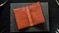 Brown leather wallet on a dark surface with tools in the background